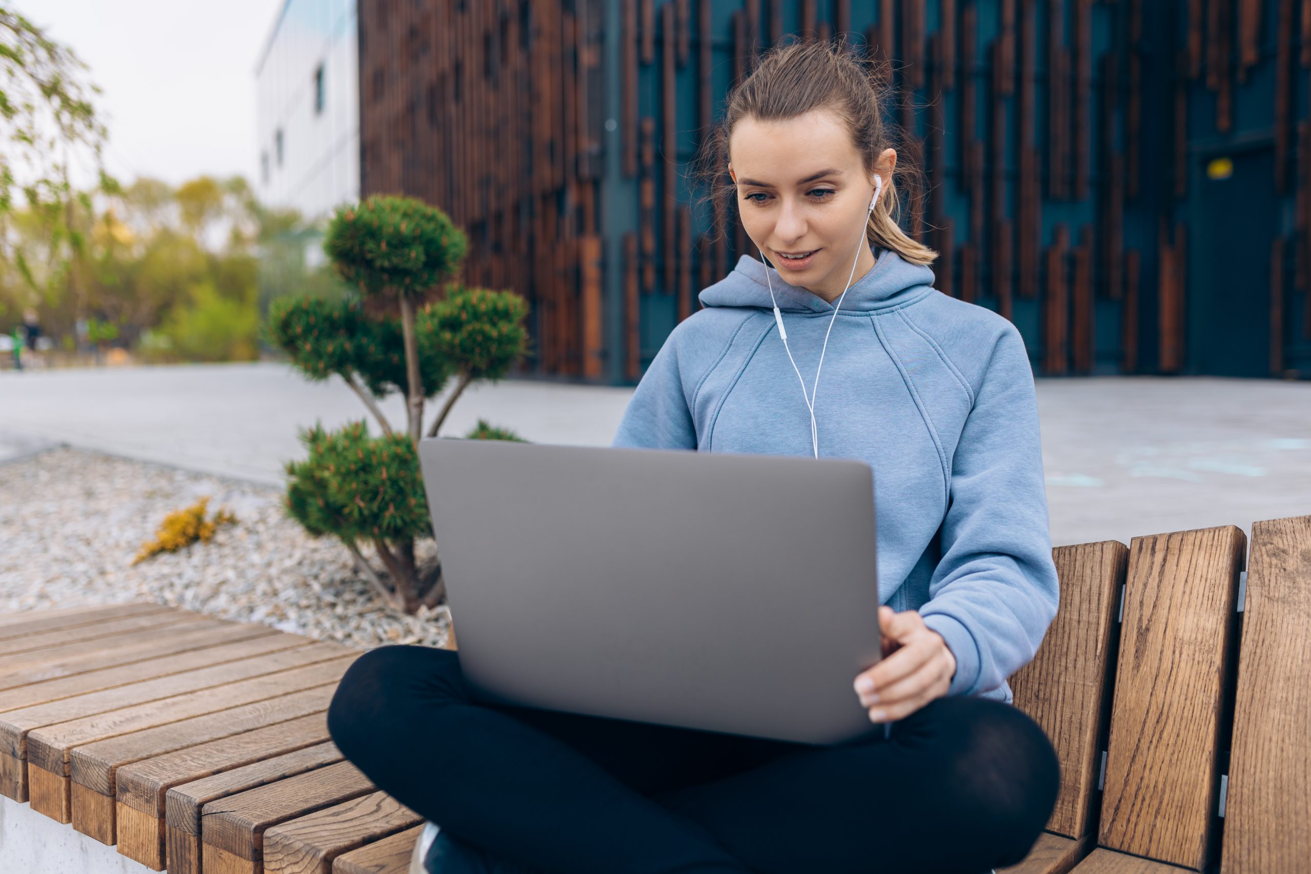 Front view of girl with earphones talking, using webcam. Blonde pretty female with ponytail making video call, looking at screen, student, freelancer. Concept of modern life.